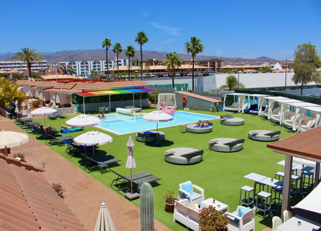 A peaceful outdoor pool area at Aqua Beach Bungalows in Maspalomas, Gran Canaria, featuring sun loungers, umbrellas, and a vibrant rainbow canopy.