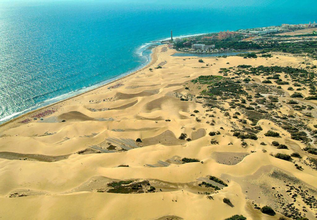 Aerial view of the Maspalomas Sand Dunes, with golden sand formations and the Atlantic Ocean in the background, highlighting the natural beauty of Gran Canaria.