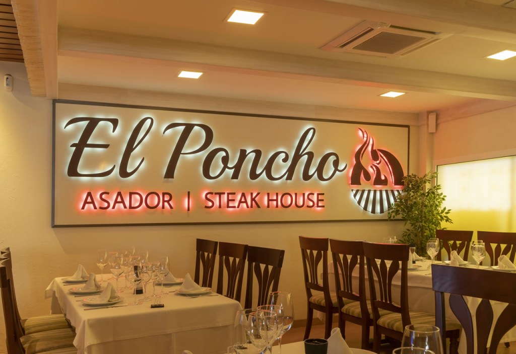 Interior of El Poncho Asador Steakhouse featuring a stylish dining setup with a prominent sign displaying the restaurant's name.